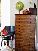 A globe on top of a chest of drawers with a stack of butterfly chairs beside it