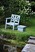 A wooden chair and a table by a garden pond