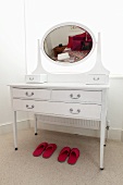 A white make-up table with an oval mirror and two pairs of pink slippers