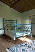 Ein blaues schmiedeeisernes Bett in einem Schlafzimmer mit Terrakottaboden