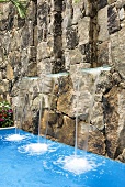 A pool with mini waterfalls coming from a natural stone wall