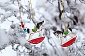 Small wooden rocking horse hanging on a snow-covered tree