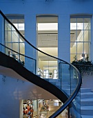 Curved exterior staircase in the twilight and a view into an illuminated loft like apartment