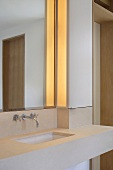 Sharp edges in a modern bathroom with illumination beside a wall mirror over a minimalist countertop
