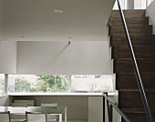 Minimalist living room with stairway made of dark wood steps and table with chair in front of window