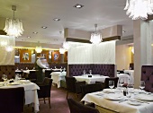 Tables set in a hotel restaurant and seats upholstered in dark leather in front of a room divider covered in fabric
