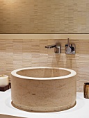 Circular sink made of beige stone and wall fitting on a wall covered in sand colored tiles