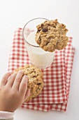 Child's hand reaching for cookie beside glass of milk