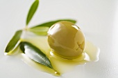Grüne Olive mit Olivenöl und Olivenblätter (Nahaufnahme)
