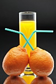 Tangerines with straws in front of a glass of juice