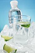 A glass of water and a bottle with limes on ice