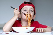 A little boy eating spaghetti with tomato sauce