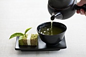 Green tea being poured with a piece of tea cake next to the cup