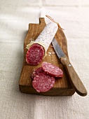 A salami on a chopping board, sliced
