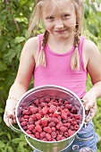 A blonde girl holding a bucket of raspberries