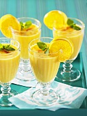 Four peach smoothies in stemmed glasses with lemon slices