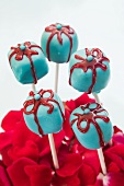 A blue parcel-shaped cake pop with a red iced bow stuck in a sea of rose petals