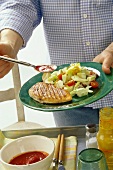 Man putting ketchup on barbecued turkey escalope with salad