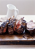 Four barbecued ribeye steaks on a wooden board