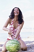 Junge Frau zerschneidet eine Wassermelone am Strand