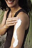 Young woman putting lotion on her arm