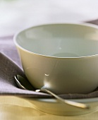 White soup bowl and spoon on violet-coloured napkin