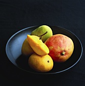 Verschiedene Mangos auf schwarzem Teller