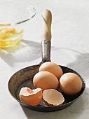 Vier braune Eier, eines aufgeschlagen, in Pfanne