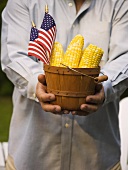 Man holding woodchip basket full of corn cobs with US flags