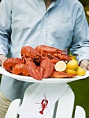 Man serving lobsters with lemons on platter (USA)