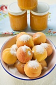 Aprikosen mit Zucker in Schüssel, dahinter Marmeladengläser