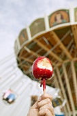 Hand with toffee apple in front of carousel (Oktoberfest, Munich)