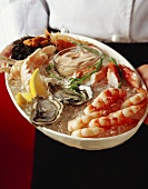 Hands holding mixed seafood platter with cocktail sauce