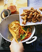 Preparing noodles with chicken fillet and vegetables in wok
