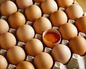 Brown eggs in egg tray, one egg broken open