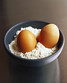 Two eggs in a bowl of flour