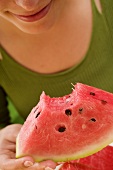Woman holding piece of watermelon with a bite taken