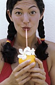 Junge Frau trinkt Cocktail mit Strohhalm aus Fruchtschale