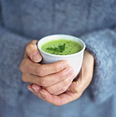 Hands holding small bowl of creamed pea soup
