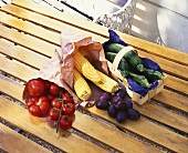 Plums, tomatoes, corncobs and courgettes in paper bags