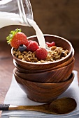 Pouring milk onto muesli and berries in cereal bowl