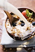 Pouring milk onto berry muesli in a cereal bowl
