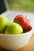 A bowl of apples beside a computer