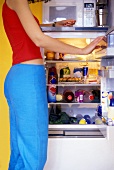 Junge Frau kontrolliert Inhalt des Kühlschranks