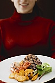Woman holding plate of Surf & Turf (beef steak with prawn)