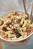 Woman holding a bowl of pasta salad with tomatoes & olives