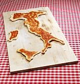 Pizza in the shape of the map of Italy on chopping board