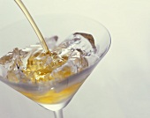 Cocktail ins Glas mit Eiswürfeln abseihen