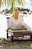 Blond woman with a plate of fruit on the beach