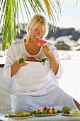 Blonde Frau isst Wassermelone am Strand